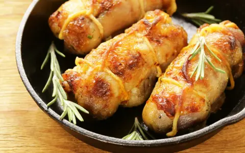 Involtini di pollo dorati e succulenti, legati con spago da cucina e guarniti con rametti di rosmarino, in una padella di ghisa.