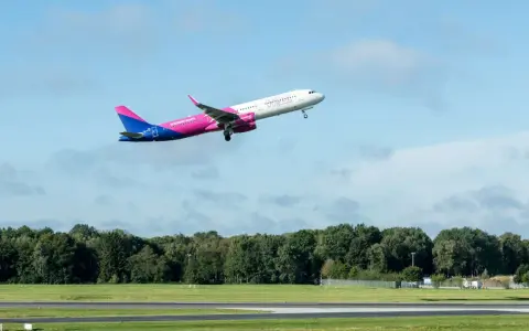 Samolot Wizz Air wznosi się na tle błękitnego nieba z chmurami.
