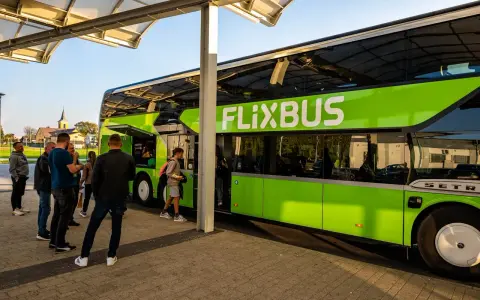 Zielony autobus FlixBus na przystanku, z pasażerami wsiadającymi i wysiadającymi.