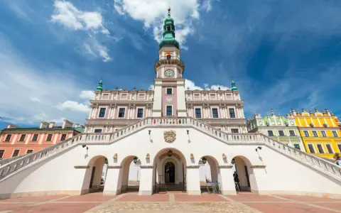 Zamość rynek: Ratusz z imponującymi schodami i kolorowe kamienice pod błękitnym niebem.