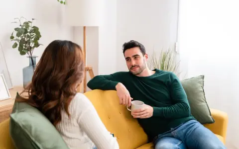 Coppia sul divano, lui con tazza in mano, lei di spalle. Una conversazione tesa, forse legata a **ADHD e tradimento**.