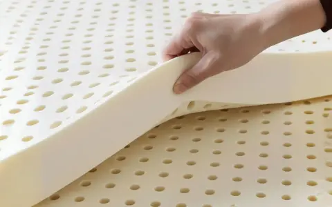 Une main soulève une couche de **latex matière** perforée, révélant sa texture aérée et souple.