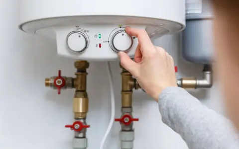 Main d'une personne ajustant le thermostat d'un chauffe-eau, contrôlant la pression de l'eau et la température.