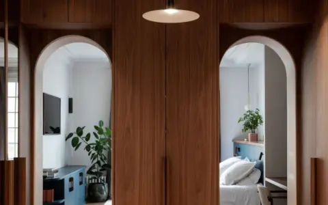Deux arches arche maison en bois de noyer encadrent une chambre avec un lit blanc et un salon avec une télévision.