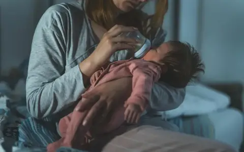 Mama karmi butelką niemowlę, które obudziło się w nocy z płaczem.