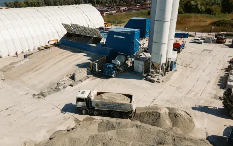 Beton skład z ciężarówką wyładowującą materiał. W tle silosy i budynki przemysłowe.