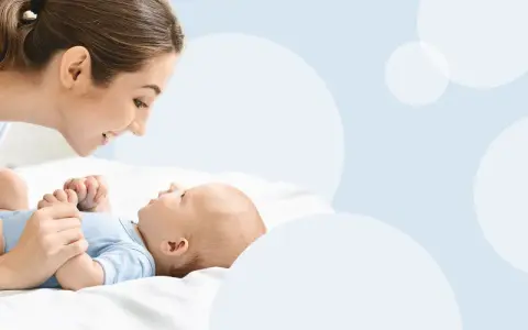 Uśmiechnięta mama pochyla się nad dzieckiem, które świadomie mówi "mama".