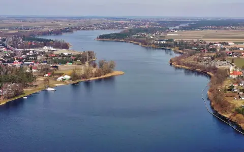 Rozległe jezioro Mikorzyńskie otoczone zabudowaniami i polami. W oddali widać kościół i cmentarz.