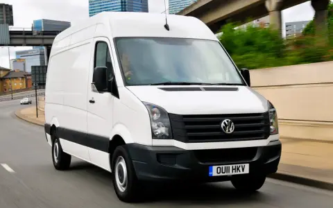 Biały Volkswagen Crafter 2.5 TDI w ruchu miejskim, z widocznymi budynkami w tle.