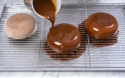 Dolce lucido ricoperto da una colata di cioccolato. La glassa scende sui lati, creando un effetto invitante.
