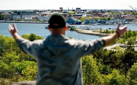 En person med armarna utsträckta njuter av utsikten över en hamn och stad, kanske den soligaste staden i Sverige.