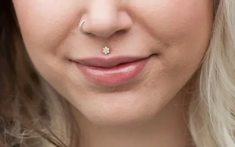 Delikatny labret co to? To ozdoba wargi w kształcie kwiatka z cyrkoniami. Obok kolczyk w nosie.