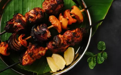 Brochettes de poulet grillées, marinées et savoureuses, avec oignons et poivrons, servies sur une feuille de bananier avec des quartiers de citron.