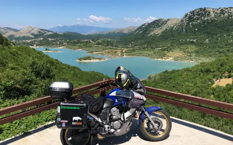 Moto pronta per avventurosi giri in moto nel Lazio, con un panorama mozzafiato sul lago turchese e le montagne verdi.