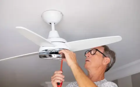 Hombre con gafas ajusta un ventilador de techo pladur con un destornillador.