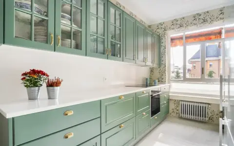 Encantadoras cocinas verdes vintage con armarios de cristal y detalles dorados. Flores rojas y naranjas adornan la encimera blanca.