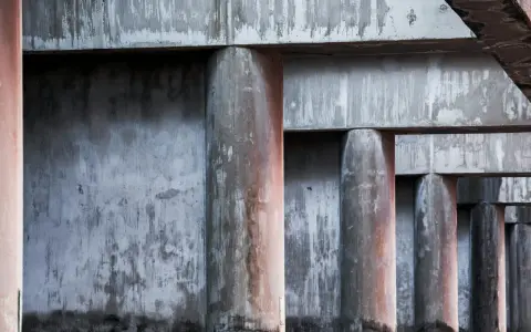 Columnas de hormigón con textura rugosa y marcas de agua, parte de un forjado de hormigón.