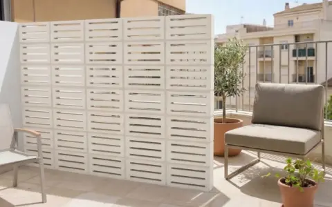 Muros cortina de bloques blancos con diseño de listones horizontales, creando un espacio exterior moderno con silla y plantas.