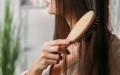 Eine Frau kämmt ihr langes, dunkles Haar mit einer Holzbürste. Sie achtet auf ihre Haare, um Haarausfall bei Frauen im Alter vorzubeugen.
