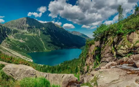 Majestatyczne tatry szczyty otaczają turkusowe Morskie Oko. Chmury na niebie dodają dramatyzmu krajobrazowi.