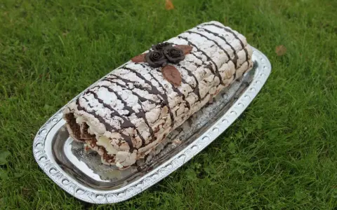 En läcker Budapestrulle med choklad och grädde, dekorerad med chokladrosor och pudersocker. Perfekt för ett sommarfika!