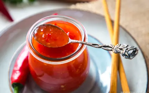 Ein Löffel mit leuchtend roter Thai Chilli Sauce, daneben frische Chilis und Stäbchen.