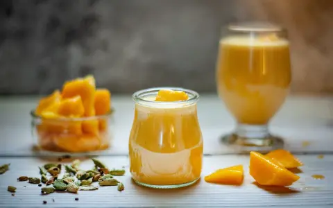 Deser z mango lassi kontra mus z marakui. Dwa pyszne, żółte desery w szklanych naczyniach, obok świeże kawałki mango i kardamon.
