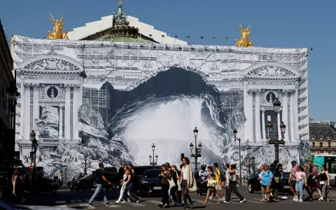 Des passants traversent devant l'Opéra Garnier, dont la façade est recouverte d'une bâche monumentale simulant des travaux et une arche rocheuse.