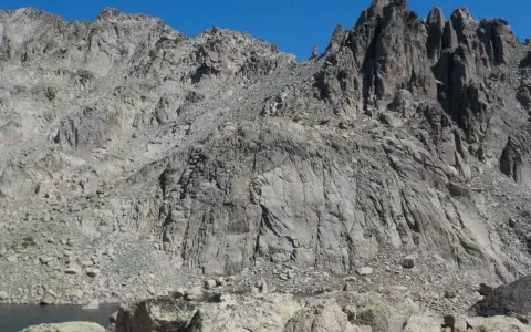 Vetta frastagliata di un monte rotondo, con rocce grigie e un lago alpino sullo sfondo.