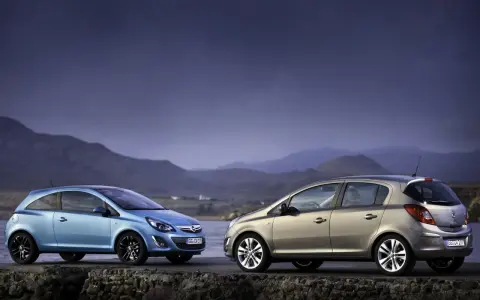 Dwa samochody Opel Corsa D, jeden niebieski, drugi beżowy, stoją na kamiennym murze nad wodą.
