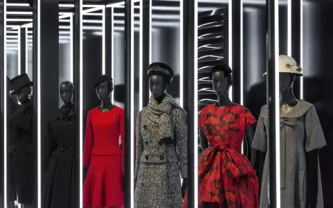 Manichini con abiti eleganti, un omaggio all'eleganza e all'origine Dior. Rossi, neri e grigi, con cappelli e sciarpe.