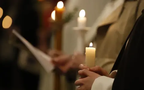 Dłonie trzymają płonące świece, symbolizujące poświęcenie ognia podczas uroczystości.