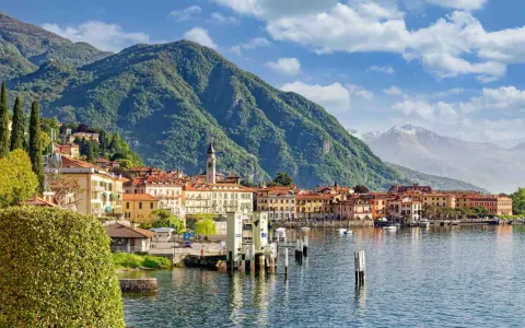 Vista di un paese sul lago d'Iseo, con montagne verdi sullo sfondo. La profondità del lago d'Iseo è suggerita dalla vastità dell'acqua.