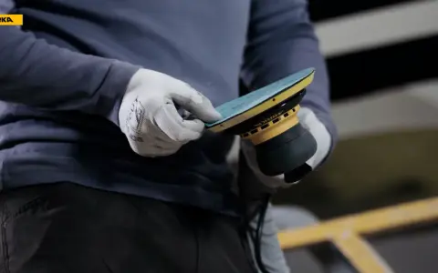 Gants blancs ajustant un disque sur une ponceuse Mirka, prêt à polir la coque d'un bateau.