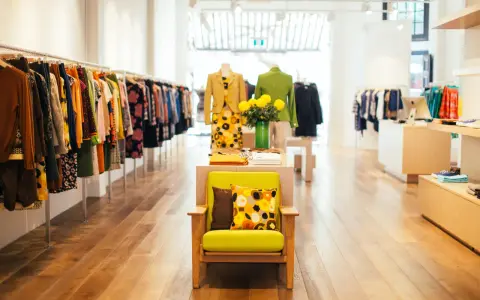 Interior de un showroom de ropa con percheros llenos de prendas coloridas y un sillón verde con cojines estampados.
