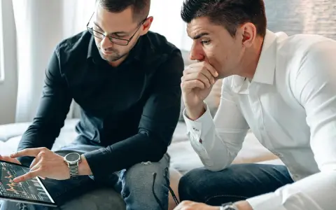Dos hombres analizan gráficos en una tablet. Uno señala la pantalla, discutiendo cómo domiciliar la nómina para optimizar finanzas.
