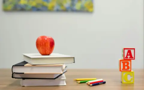 Stos książek z jabłkiem, kredki i kostki z literami A, B, C. Idealny zestaw do nauki, by stworzyć list po angielsku.