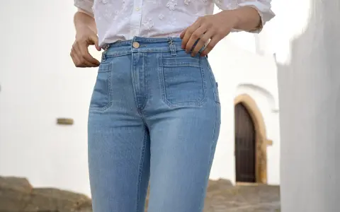 Mujer con vaqueros de tiro alto y camisa blanca, ajustándose la cintura.
