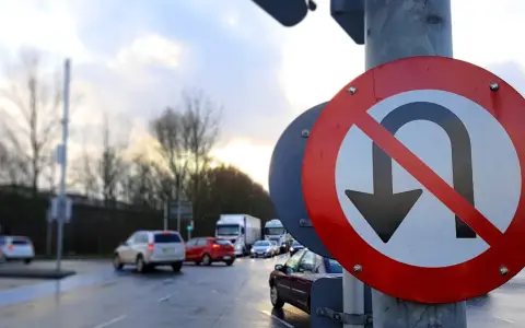 Znak zakazu zawracania na skrzyżowaniu. Samochody stoją w deszczu, czekając na zielone światło.