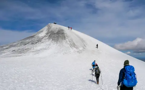 Vandrare klättrar uppför en snöig sluttning mot Kebnekaises topp. En bra packlista för Kebnekaise är avgörande för en säker och njutbar tur.
