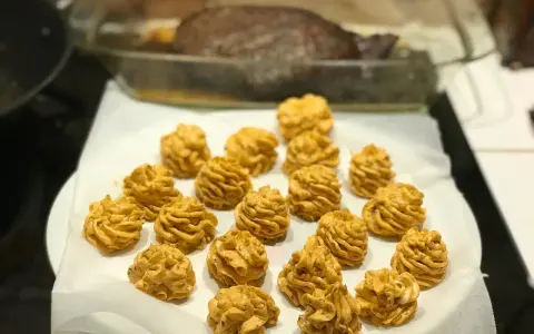 Piped dollops of golden-brown sauce arranged on white parchment paper, with a roasted dish in the background.