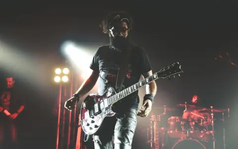 Un guitariste charismatique d'un groupe de rock mythique, en pleine performance sur scène, éclairé par des projecteurs.