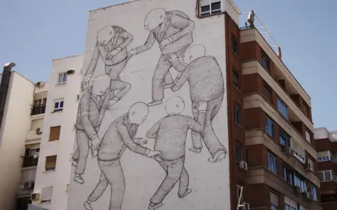 A striking street art style mural depicts a group of bald figures in suits, seemingly engaged in a peculiar, interconnected dance or struggle on a building's facade.