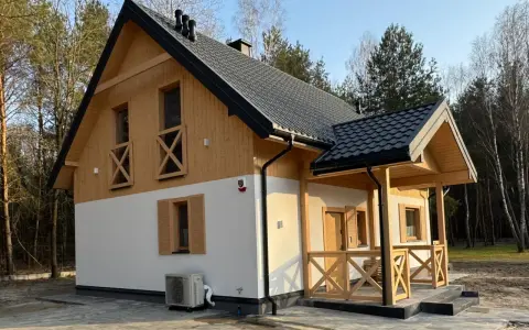 Nowy dom w lesie, drewniane elementy i biały tynk. Prowadzenie budowy domu zakończone sukcesem, gotowy do zamieszkania.