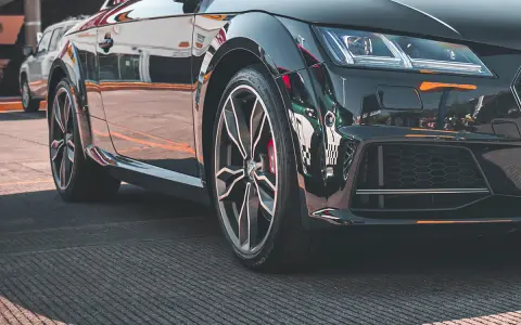 Błyszczące, czarne auto sportowe z felgami i widocznym rantem ochronnym opony.