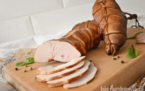 Wędzona pierś z kurczaka, pokrojona w plastry, leży na desce obok całych kawałków, przyprawiona pieprzem i ziołami.