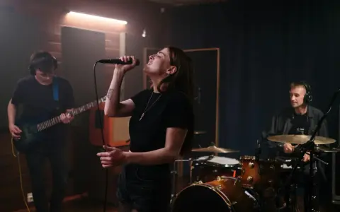 Wokalistka z pasją śpiewa w zespole, podczas gdy gitarzysta i perkusista tworzą rytm w studiu nagraniowym.