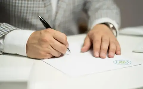 Mężczyzna w eleganckim garniturze podpisuje dokument, który może być wpisem do księgi wieczystej.