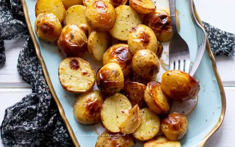 Patate novelle al forno dorate e croccanti, servite su un piatto decorato, pronte per essere gustate.