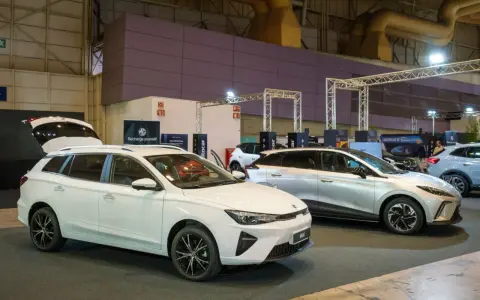 Białe kombi MG5 z otwartą klapą bagażnika i srebrny SUV na wystawie samochodowej.